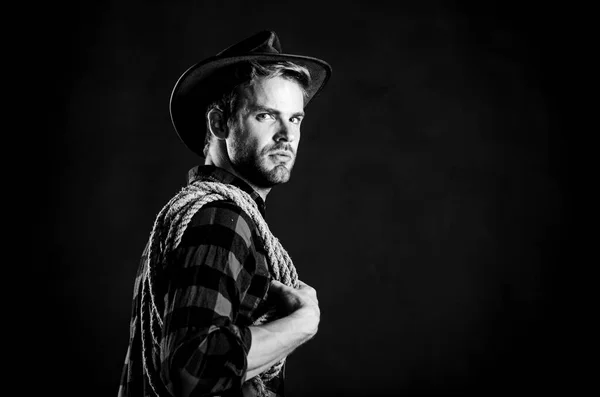 Homem unshaven cowboy fundo preto. Lasso é usado em rodeios como parte de eventos competitivos. O laço pode ser amarrado ou embrulhado. A vida ocidental. Homem de chapéu segura corda. ferramenta laço de cowboy americano — Fotografia de Stock