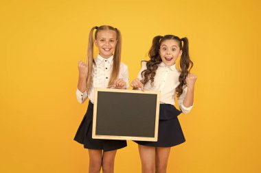 Bilgi vermek. Küçük çocuklar sarı arka plan hakkında bilgi için boş tahta ile evet jest yapıyor. Düzenli bilgi panosu olan küçük kız öğrenciler. Mutlu bilgileri paylaşma, kopyalama alanı