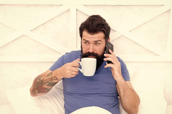 Yatakta mobil teknoloji kullanan sakallı bir adam. Telefonda konuşan ve evde kahve içen yakışıklı bir adam. Modern yaşam yeni teknolojisi. Teknoloji konsepti. Hoş sohbetti. İyi sabahlar. Merhaba canım. — Stok fotoğraf