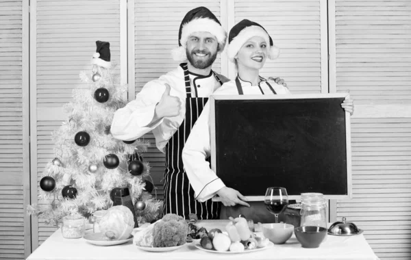 Man en vrouw de kerstmuts van chef-kok in de buurt van de kerstboom houden schoolbord kopie ruimte. Koppel de ingrediënten van de lijst van het selectievakje voor kerstdiner. Kerst recept concept. Menu voor onze familie. Kerst maaltijd koken — Stockfoto