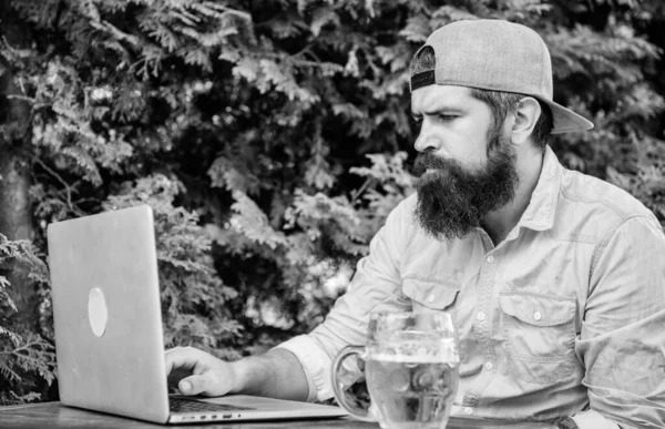 Finalmente sexta-feira. Hipster relaxar sentar terraço com cerveja. Freelancer hipster barbudo desfrutar do fim do dia de trabalho com caneca de cerveja. A cerveja ajuda-o a relaxar depois de um dia difícil. Brutal homem lazer com cerveja e laptop — Fotografia de Stock