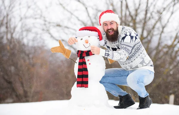 Juegos de invierno. Actividad invernal. Diversión y entretenimiento. Vacaciones de invierno. Hombre hizo muñeco de nieve. Hipster con barba al aire libre. Hombre con sombrero de Santa Divirtiéndose al aire libre. Chico feliz cara nieve naturaleza fondo — Foto de Stock