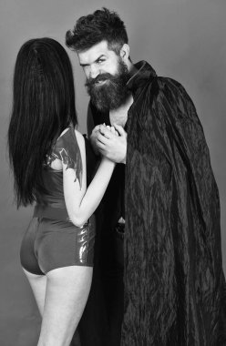 Cadılar Bayramı konsepti Şeytani yüzlü çift rol yapıyor. Pelerinli vampir ve seksi şeytan kız el ele tutuşuyor. Vampir, şeytan, kırmızı arka plan gibi giyinmiş kadın ve erkek. Birbirine aşık çift, mükemmel bir eş..