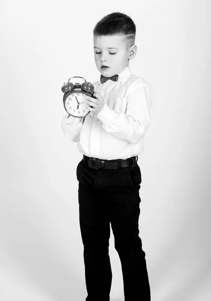 Niño feliz con reloj retro en corbata de lazo. Hora de la fiesta. Empresario. Ropa formal. Gestión del tiempo. Buenos días. niño pequeño con despertador. Es hora de relajarse. Esmoquin. Feliz infancia. Buen comienzo de la mañana —  Fotos de Stock