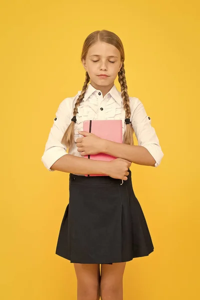 Littérature pour l'école. Adorable petite fille aux yeux fermés tenant un livre de littérature anglaise sur fond jaune. Petit enfant mignon appréciant la littérature pour enfants. Préparation à un examen de littérature — Photo