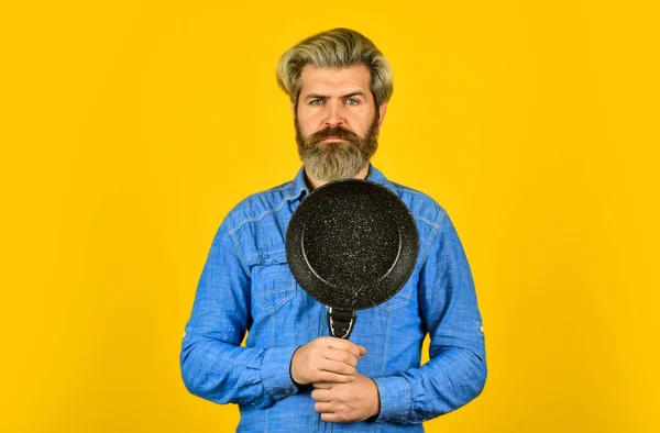 Repas de friture. Parfait pour faire des crêpes. Vases de cuisson en fonte émaillée. Des ustensiles de cuisine. Poêle antiadhésive surface en porcelaine. Un homme tient la poêle. Cuisiner des aliments sains. hipster barbu préparer le petit déjeuner — Photo