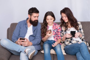 Oyun uygulaması oynat. Çevrimiçi aile. Anne baba ve kızı kanepede dinleniyor. Aile hafta sonunu internette geçiriyor. Küçük bir kız çocuğu, ailesine karşı akıllı telefon kullanıyor. İnternette aile sörfü. Aile eğlencesi.