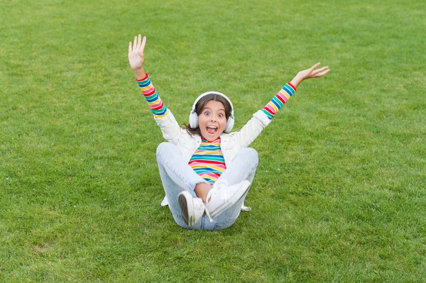 Kid girl enjoy music green grass meadow. Happiness is not something you sit back and wait. Listen music while relaxing outdoor. Child headphones listen music. Cool girl headphones listening music