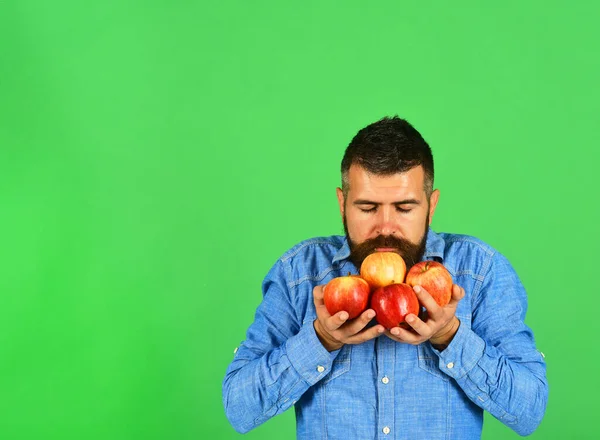 Hombre con barba huele fruta roja aislada sobre fondo verde — Foto de Stock