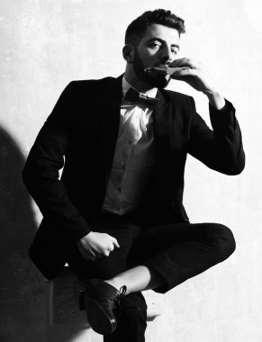 Sakallı adamın elinde matara, stüdyo duvarında ciddi bir yüz var.