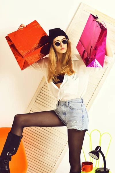 Pretty sexy woman in sunglasses at colorful chair with package — Stock Photo, Image