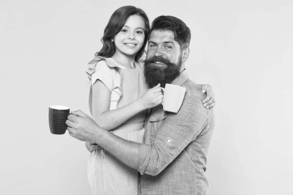 Good morning. Having coffee together. Healthy lifestyle. Family drinking tea. Bearded man and happy girl holding mugs. Father and daughter hot drink. Drink water. Drink fresh juice. Breakfast concept