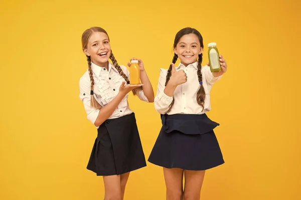 La mejor bebida para tu cuerpo. Chicas felices sosteniendo botellas de bebida de vitaminas sobre fondo amarillo. Niños pequeños sonriendo con una bebida jugosa natural y saludable. Niños pequeños disfrutando de la bebida de fruta fresca —  Fotos de Stock