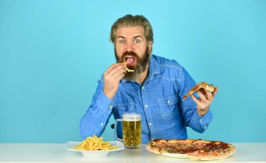 Pizzacı. Pizza partisi konsepti. Mutluluğu ağıza vermek. Bira ve yemek. Neşeli sakallı hippi adam pizza yiyor. Barda akşam yemeği. Aç adam pizza yiyecek ve bira içecek.