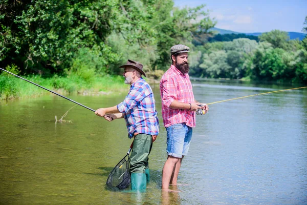 good team. hobby and sport activity. Trout bait. father and son fishing. two happy fisherman with fishing rod and net. male friendship. family bonding. summer weekend. mature men fisher
