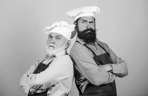 Culinary show. Restaurant staff. Culinary battle. Mature bearded men professional restaurant cooks competitors. Chef men wear aprons. Father and son culinary hobby. Cafe workers. Culinary industry