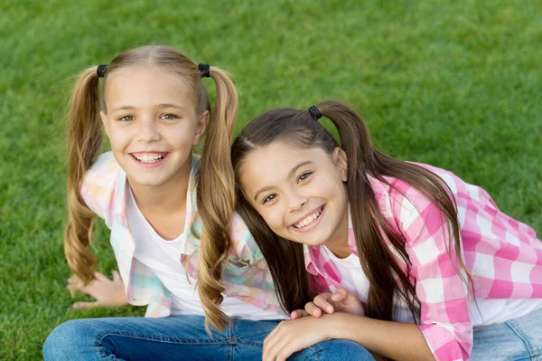 Girls rule, enjoy. Happy girls sit on green grass. Beauty look of little girls. Cute girls smile woth long hair. Beauty salon. Small children in casual style. Fashion and style. Beautiful and lovely — Stock Photo, Image