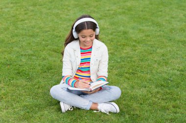 Çevrimiçi öğrenme. Eğitici podcast. Hallet şu işi. Açık havada müzik dinlemek. Çocuk müzikten hoşlanıyor. Çayır gibi otur. Keyifli zaman. Çocuk kulaklıkları müzik dinler. Havalı kız kulaklıkları müzik dinliyor.