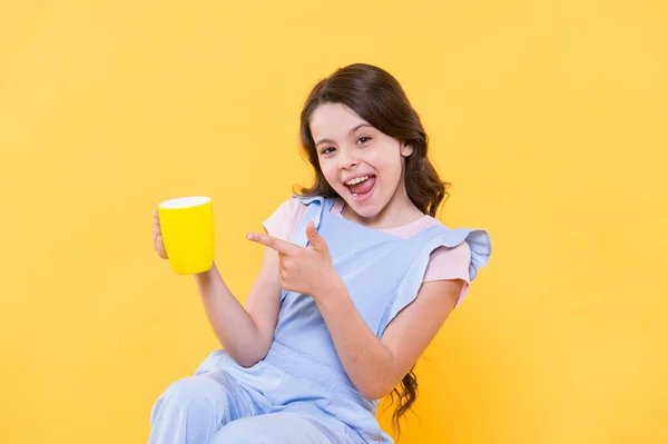 Drink it baby. Happy child point finger at cup yellow background. Little kid enjoy hot drink. Milk tea. Hot cacao or chocolate. Tasty drink recipe. Natural nutrition. Healthy dieting. Lets drink it