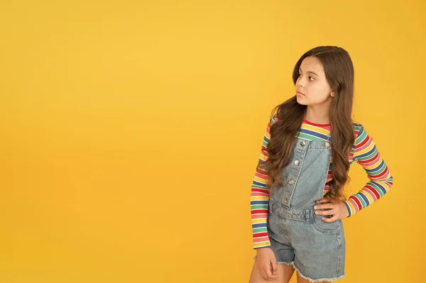 Child presenting product, copy space. Happy childrens day. childhood tips. hipster girl colorful clothes. optimist concept. small girl yellow background. summer kid fashion. advertisement concept — Stock Photo, Image