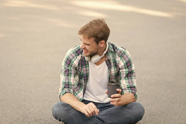 Bom dia, café. estudante relaxar e recarregar. Café para levar. O tipo bebe café ao ar livre. Sente-se no chão. estudante em fone de ouvido. educação online. ouvir música. conceito ebook. homem camisa xadrez — Fotografia de Stock