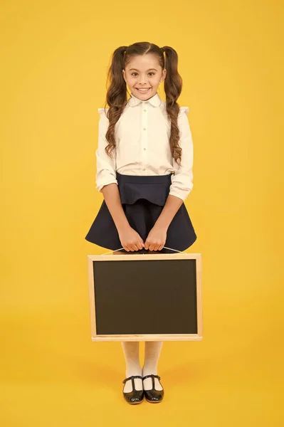 Entregando nueva información. Alumna alegre colegiala informándote. El uniforme escolar femenino sostiene la pizarra. De vuelta a la escuela. Niña de la escuela mantenga espacio en blanco pizarra copia. Anuncio y promoción — Foto de Stock