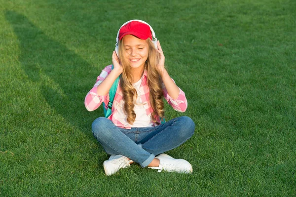 Ouça música enquanto relaxa ao ar livre. Kid girl desfrutar de música verde grama prado. Foi um momento agradável. Os auscultadores infantis ouvem música. Auscultadores para raparigas a ouvir música. Podcast educacional. Aproveite cada momento — Fotografia de Stock