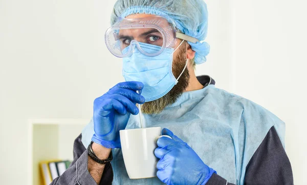 Garments placed to protect health. Infection prevention and control measures. Face protection goggles mask gloves head cover. Personal protective equipment. Guy in mask drink tea coffee using straw