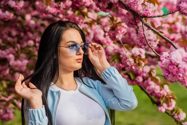 Bahar çiçeğinin açtığı süslü güneş gözlüklü kadın. Kiraz çiçekli kız. Bahar moda koleksiyonu. Sakura ağacı çiçek açıyor. Yumuşak ve yumuşak. Sakura ona yakışıyor. Muhteşem çiçek ve dişi güzellik — Stok fotoğraf