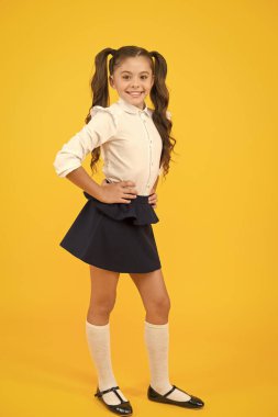 Okul tarzına geri dönmek heyecan verici. Sarı arka planda uzun at kuyruğu saçlı mutlu küçük kız. Küçük çocuk resmi bir şekilde gülümsüyor. Okul modasına bir tarz katıyor.