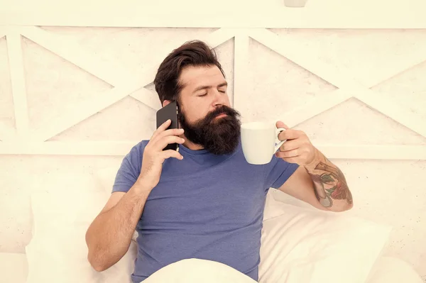 Hoş sohbetti. İyi sabahlar. Merhaba canım. Yatakta mobil teknoloji kullanan sakallı bir adam. Telefonda konuşan ve evde kahve içen yakışıklı bir adam. Modern yaşam yeni teknolojisi. Teknoloji konsepti — Stok fotoğraf