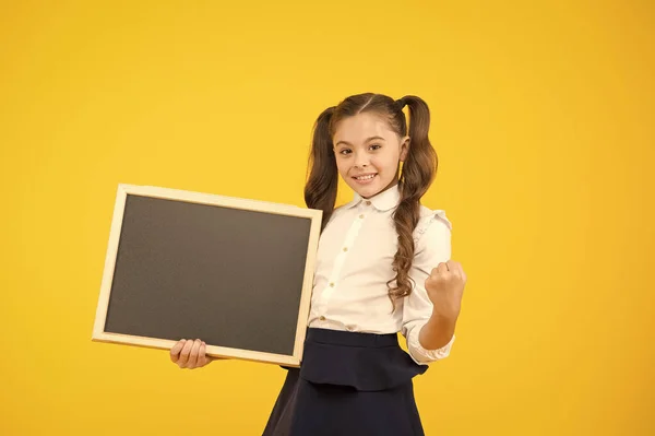 Escrevendo para a memória. Menina segurando superfície de escrita preta no fundo amarelo. Criança pequena mostrando punho com quadro para escrever informações. Placa em branco para escrever anúncio, espaço de cópia — Fotografia de Stock