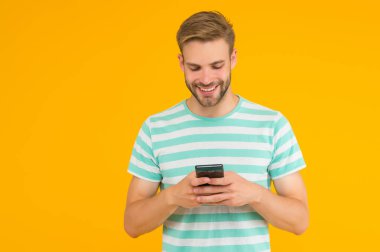 SMS mesajı gönderiliyor. Mutlu adam SMS 'i akıllı telefon sarı arka planıyla gönderiyor. SMS mesajı. Kısa mesaj servisi. Yeni teknoloji. Taşınabilir yaşam tarzı. Modern hayat. Güvenilir SMS teslimatı