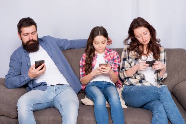 Çevrimiçi aile. Aile hafta sonunu internette geçiriyor. Küçük bir kız çocuğu, ailesine karşı akıllı telefon kullanıyor. İnternette aile sörfü. Anne baba ve kızı kanepede dinleniyor. Aile eğlencesi. Oyun uygulamasını çal