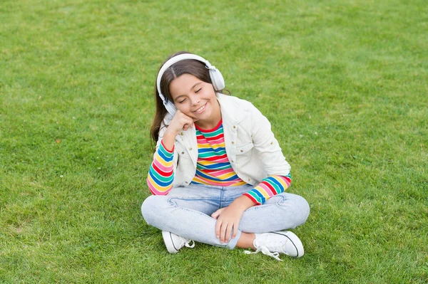 rich imagination. kid enjoy song in park nature. happy childhood concept. use digital device in modern life. schoolgirl relax outdoor. happy child listen music in earphones. small girl on green grass