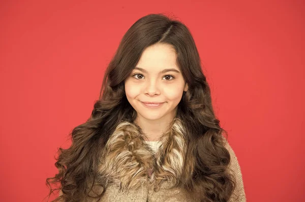 Ela é tão gira. menina bonita cabelo encaracolado longo. pequena beleza sorrindo no fundo vermelho. conceito cabeleireiro. camisola quente para a estação fria. Estilo de moda infantil. infância feliz. retrato de criança bonito — Fotografia de Stock