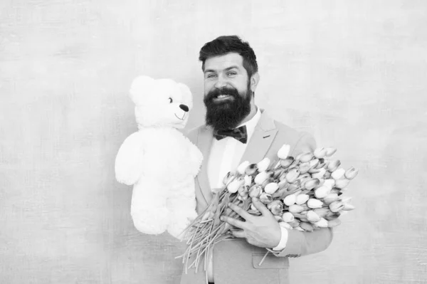 Homme barbu costume gentleman noeud papillon tenir ours en peluche et bouquet. Heureux et amoureux. Gentleman lui faisant une surprise romantique. Un cadeau romantique, messieurs. Salutations d'anniversaire. Joyeux anniversaire mon amour — Photo