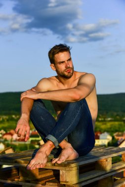 Güçlü kaslı adamın yüzünde kıllar var. Atletik vücut şekli. Tişörtsüz adam gün doğumunda rahatlar. Kaslı vücutlu genç bir atletik. Sporcu ve fitness modeli. çıplak güçlü adam