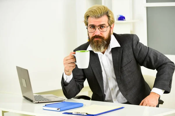 Boire du café frais. homme barbu assis au bureau. homme d'affaires brutal confiant. Élégant homme d'affaires analysant les données dans le smartphone. Quarantaine agile. avocat utiliser un cahier pour le travail — Photo