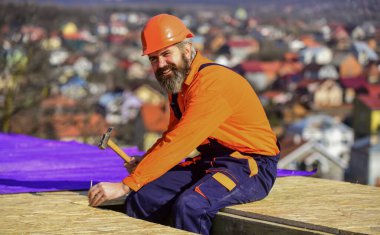 Yakışıklı inşaatçı çekiç kullanır. Profesyonel tamir çatısı. Düz çatı kurulumu. Çatı keçesi. Özel koruma giysisi içinde çatı tamircisi. İnşaat binasının altındaki yeni çatı