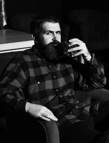 Γενειοφόρος hipster άνθρωπος κρατώντας ένα ποτήρι ουίσκι σε κόκκινη καρέκλα — Φωτογραφία Αρχείου