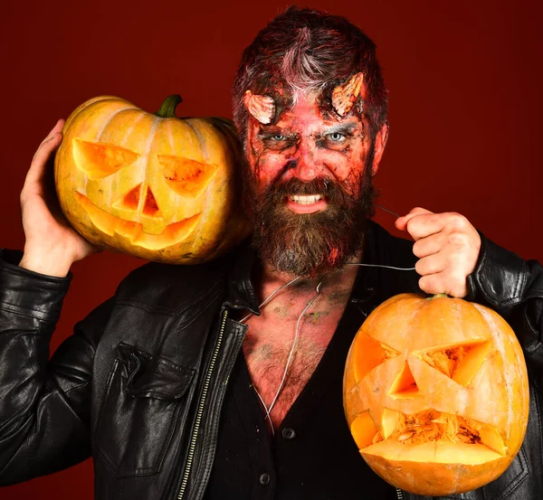 Man wearing scary makeup holds pumpkins on bloody red background.