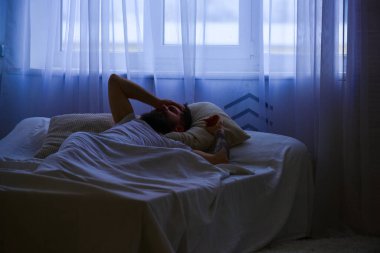 Yatakta yatan gömlekli adam, arka planda beyaz perde. Sabah uyandığında hayal kırıklığına uğramış acı çeken adam. Akşamdan kalma konsepti. Sakallı ve bıyıklı maço uyandı..