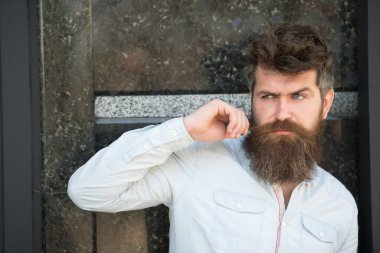 Sakallı ve bıyıklı bir adam, siyah mermer arka planda. Erkeklik kavramı. Kıvırcık saçlı hippi, mesafeye bakarken bıyık büker. Adam meraklı ve meraklı görünüyor..