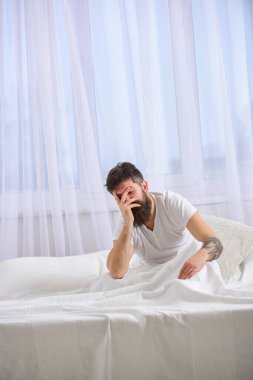 Yorgun ve uykulu bir kavram. Yatakta oturan bir adam, yatağa yaslanırken uyuyakalıyor, arka planda beyaz perdeler var. Sakallı maço uyuyor, dinleniyor, kestiriyor. Otururken uyuyan sakin yüzlü adam..