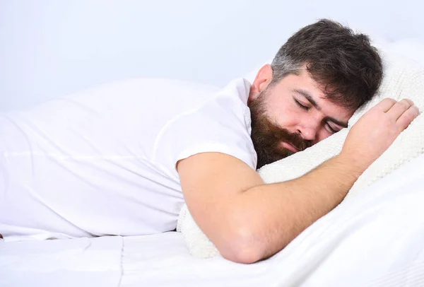 Man in shirt op bed, witte muur op de achtergrond. Een man met een rustig gezicht, slapend op witte lakens en een kussen. Slaap en siësta concept. Macho met baard en snor slapen, ontspannen, een dutje doen, rusten. — Stockfoto
