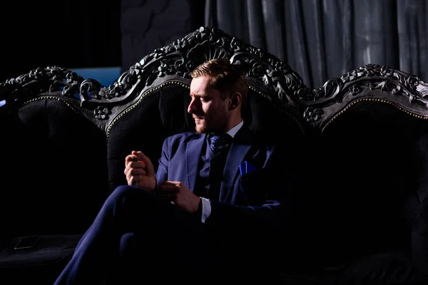 Retrato de homem de negócios adulto vestindo terno moderno e sentado estúdio moderno no sofá de couro . — Fotografia de Stock