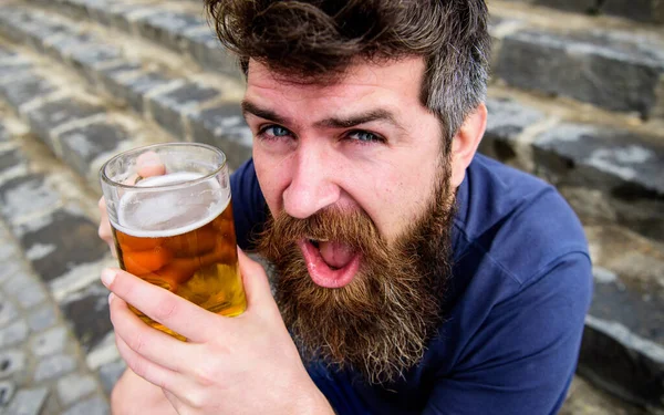 Péntek lazítás koncepció. Egy fickó, aki hideg sörrel pihen. Hipster vidám arccal sört iszik a szabadban. A szakállas és bajszos férfi poharat tart sörrel, miközben a kőlépcsőn ül. — Stock Fotó