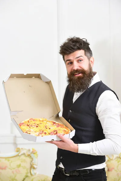 Koncepcja dostarczania pizzy. Mężczyzna z brodą i wąsami trzyma dostarczone pudełko ze smaczną, świeżą pizzą. Macho w klasycznych ubraniach głodny, na szczęśliwej twarzy, będzie jeść pizzę, luksusowe tło wnętrza. — Zdjęcie stockowe