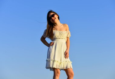 Romantik bir ruh hali. Güzel kadın güneş gözlüğü takıyor. Kadın yaz modası. Açık havada beyaz elbiseli şehvetli bir güzellik. Bahar havası. Gökyüzünde esmer saçlı seksi kız. mükemmel gün batımı veya gün doğumu